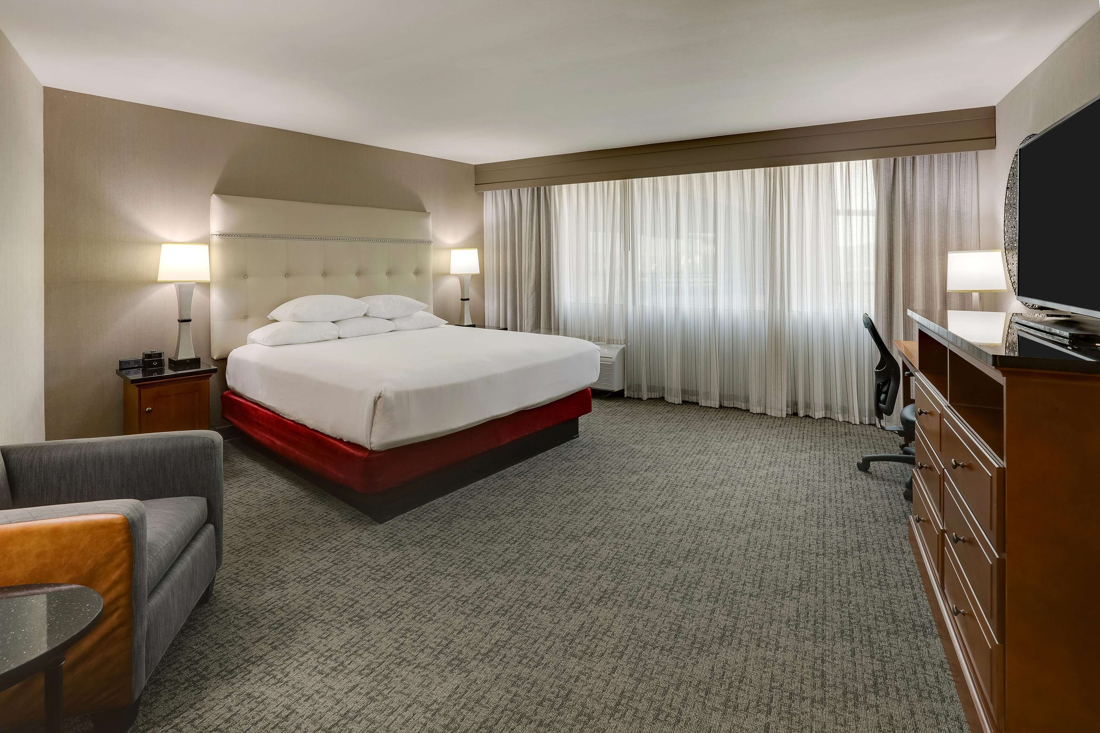A hotel room with a large bed, two bedside tables with lamps, a TV, a desk, and a chair.