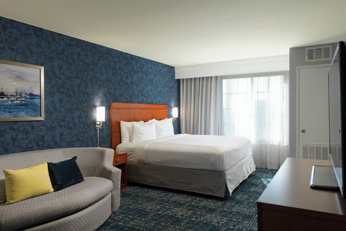 A hotel room with a bed, a sofa, a desk, and a painting on the wall.