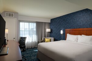 Una habitación de hotel con una cama grande, un escritorio con lámpara, una silla y una ventana con cortinas.