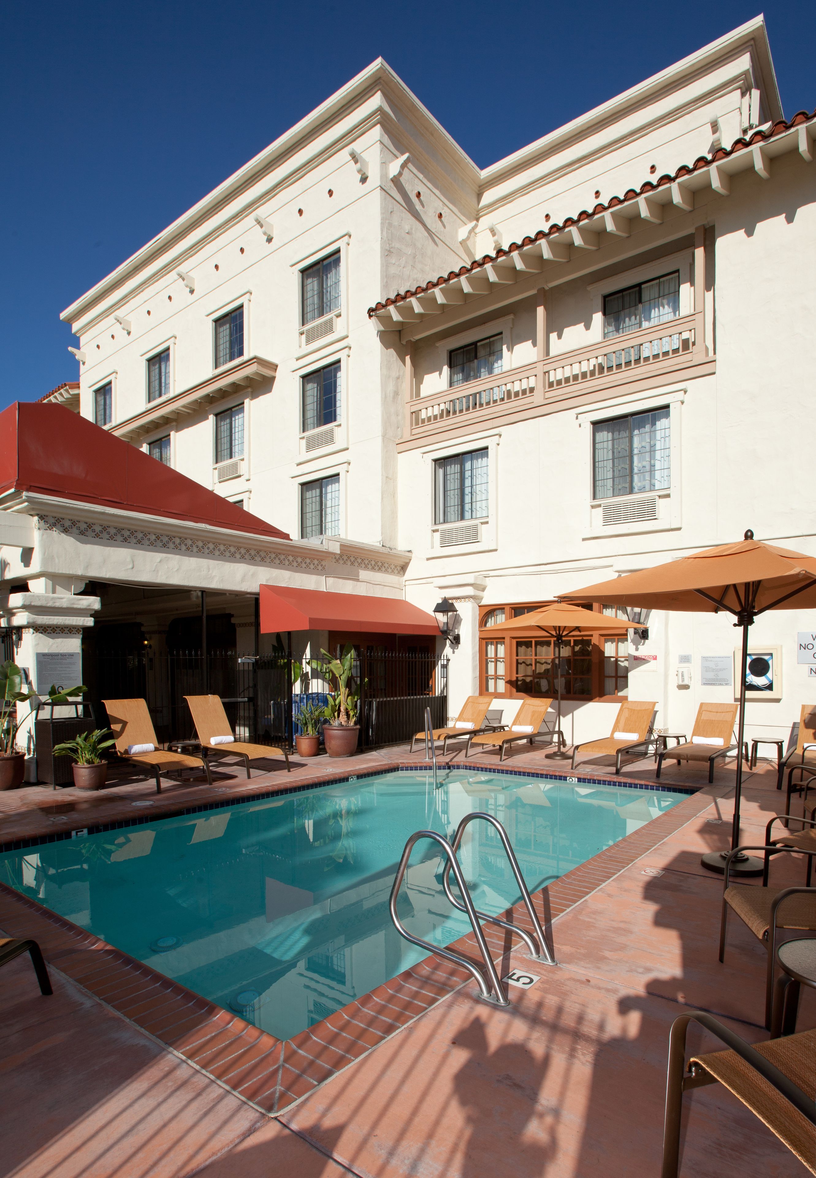 Ein Hotelpoolbereich mit Liegestühlen, Sonnenschirmen und Blumentöpfen.