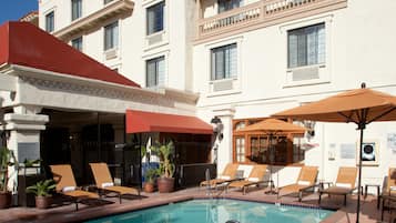 A hotel pool area with lounge chairs, umbrellas, and potted plants.