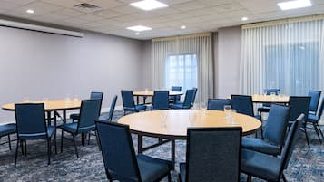Un salón de conferencias con mesas redondas, sillas azules y piso alfombrado.