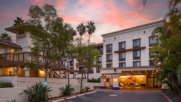 Un hotel con un amplio estacionamiento, una entrada bien iluminada y un balcón con vistas al estacionamiento.