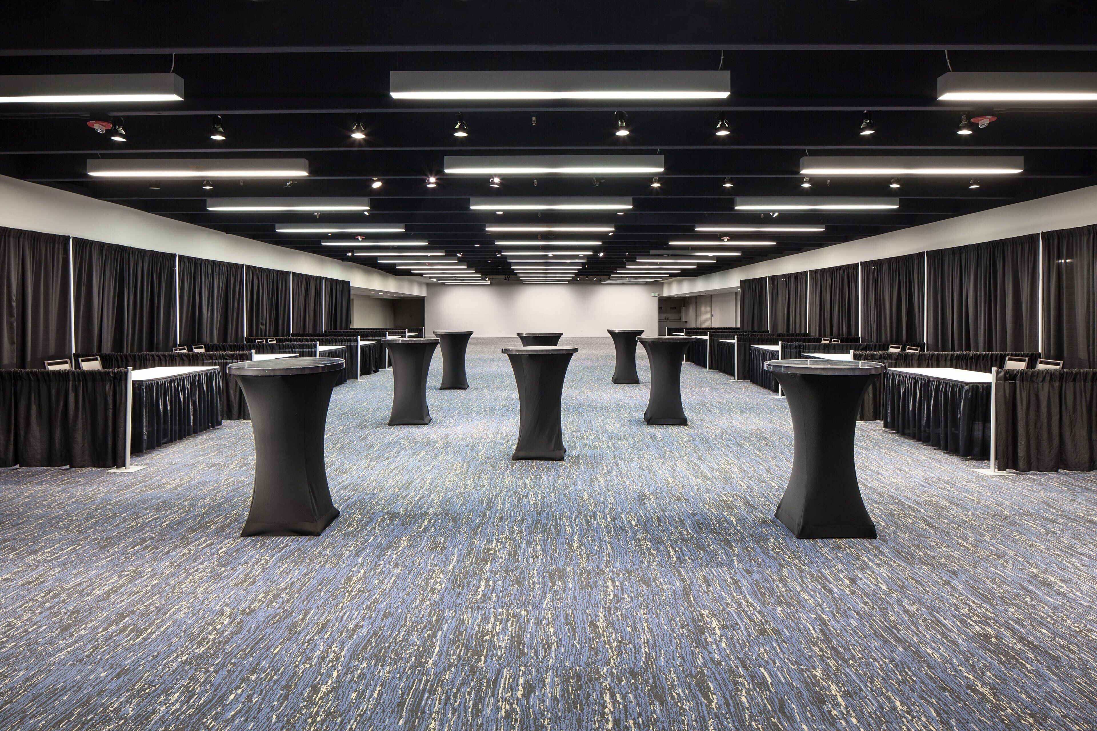 A spacious conference room with a long table and multiple chairs, a carpeted floor, and a modern ceiling design.