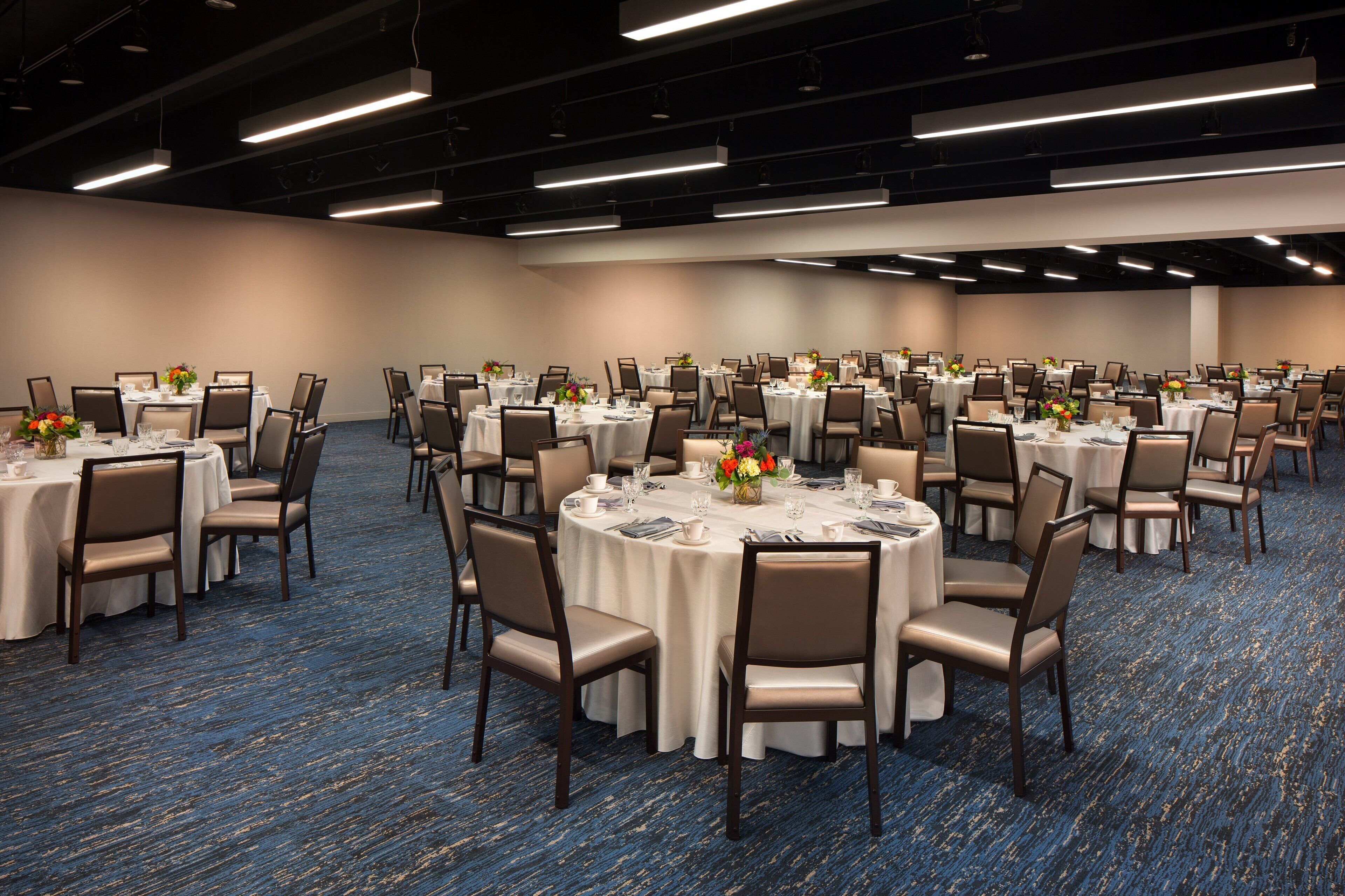 A large conference room with round tables, chairs, and floral centerpieces.