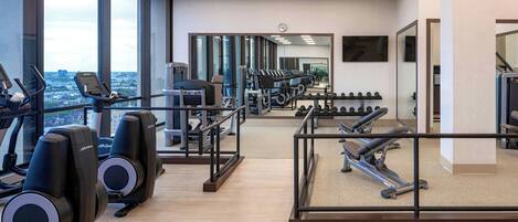 Et fitnesscenter med løbebånd, træningsmaskiner og et stort spejl, der reflekterer rummet.