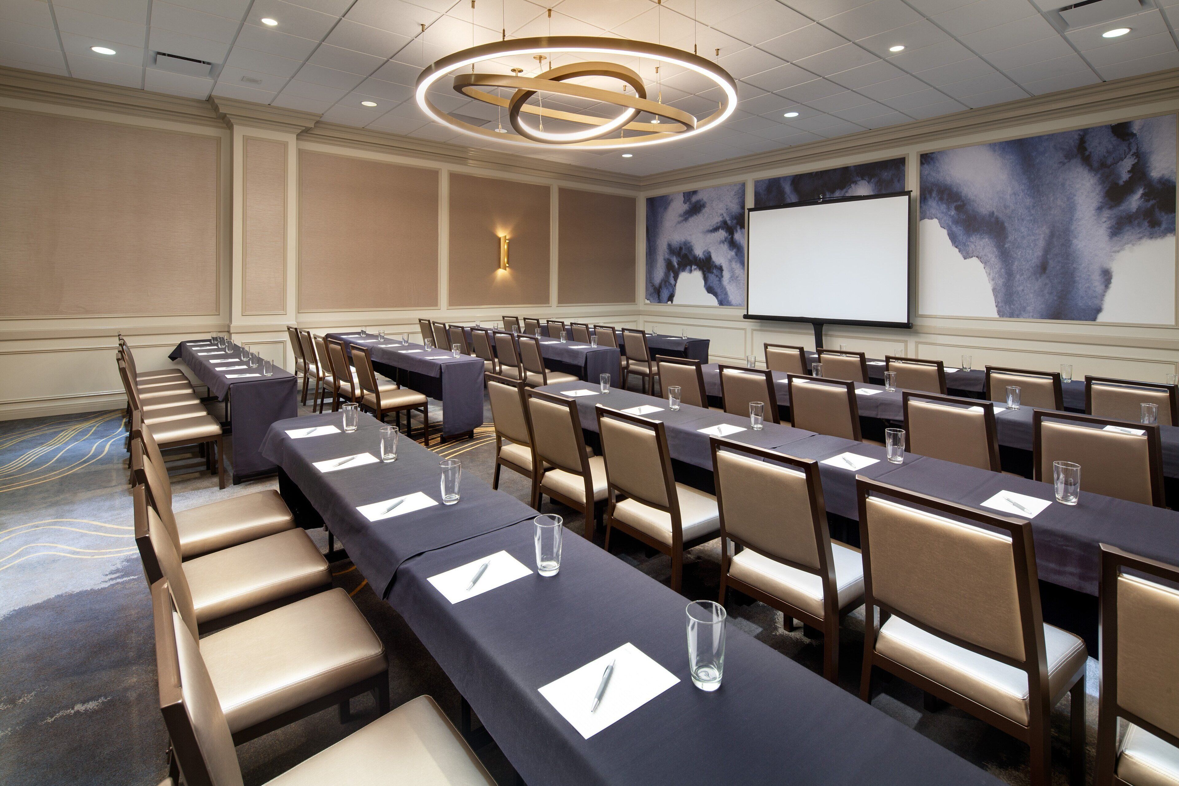 A conference room with long tables, chairs, and a projector screen.