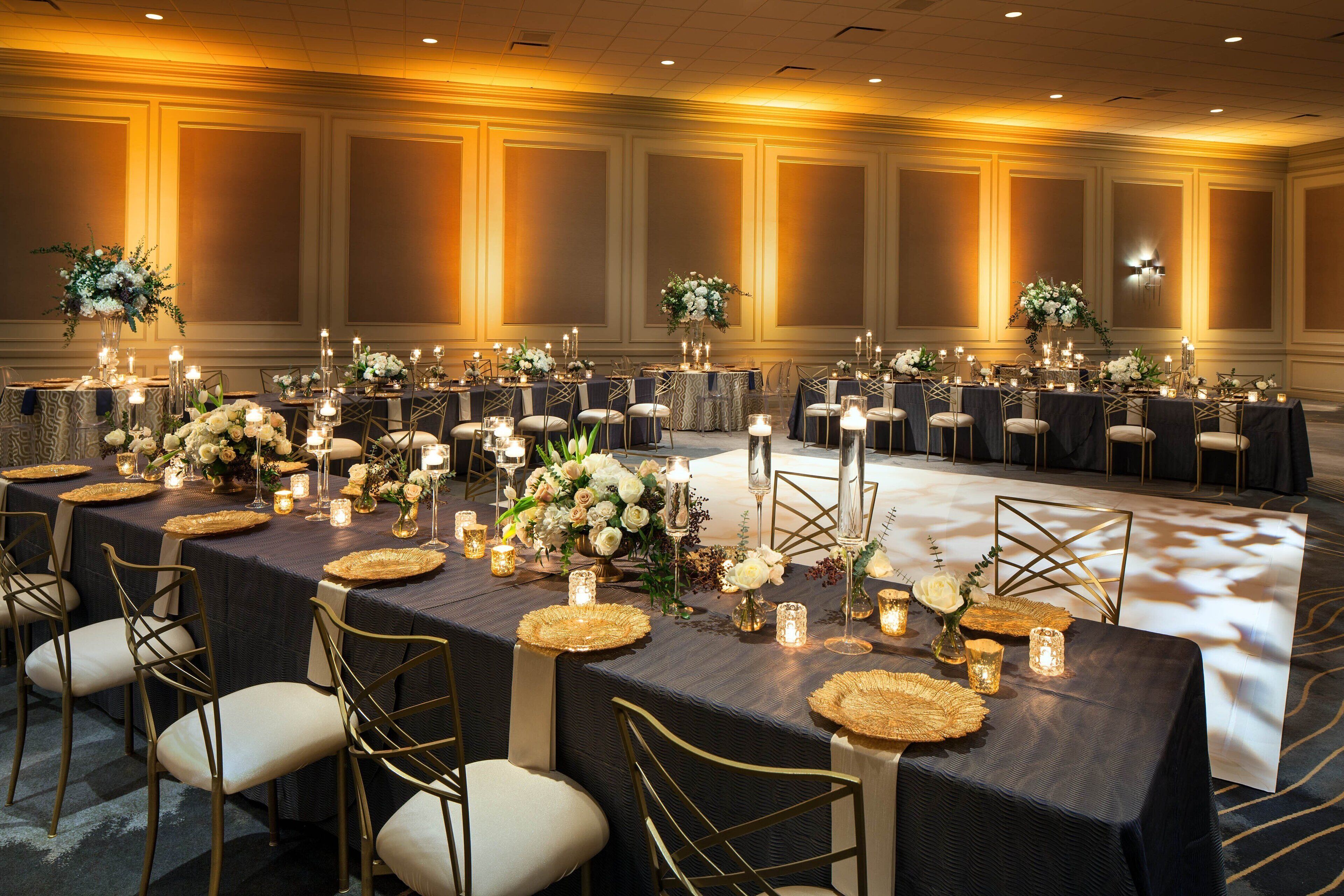 A banquet hall with tables set for a formal event, featuring floral centerpieces and candles.