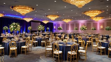 Ein Festsaal mit runden Tischen, goldenen Stühlen und üppigen Blumenarrangements.