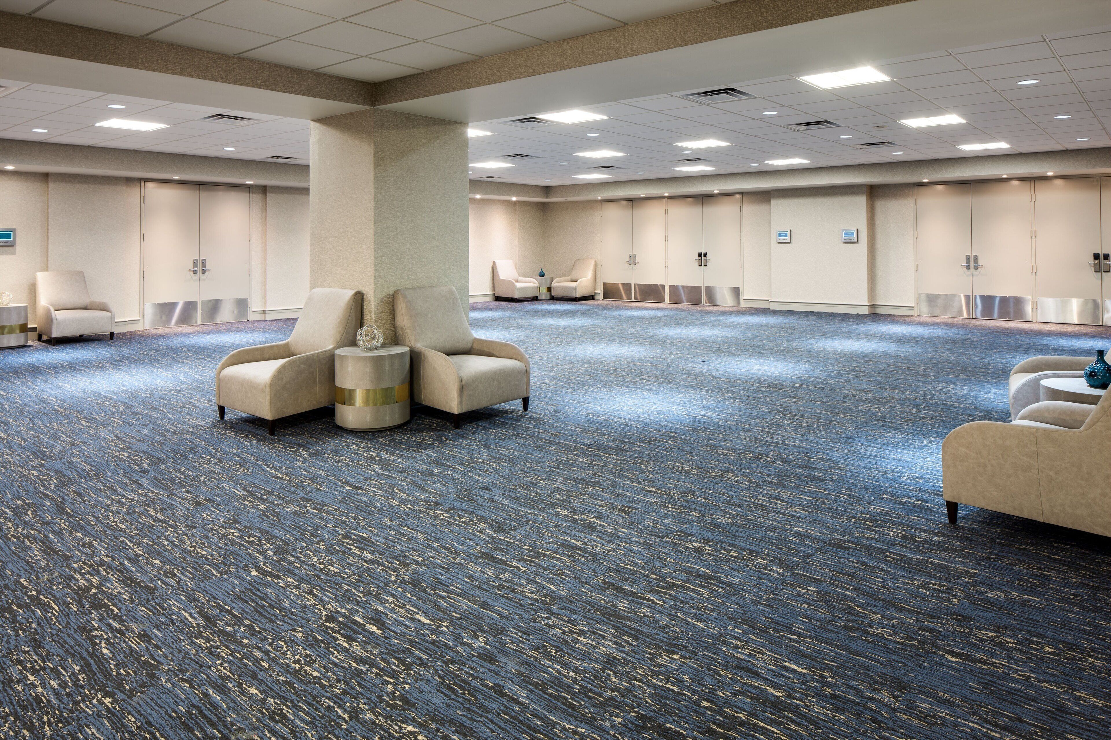 A large conference room with a blue carpet, beige armchairs, and a central pillar.