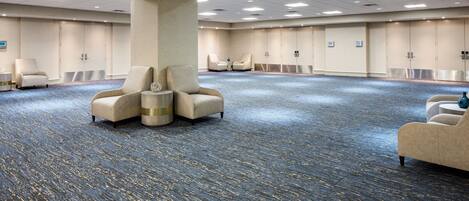 A large conference room with a blue carpet, beige armchairs, and a central pillar.
