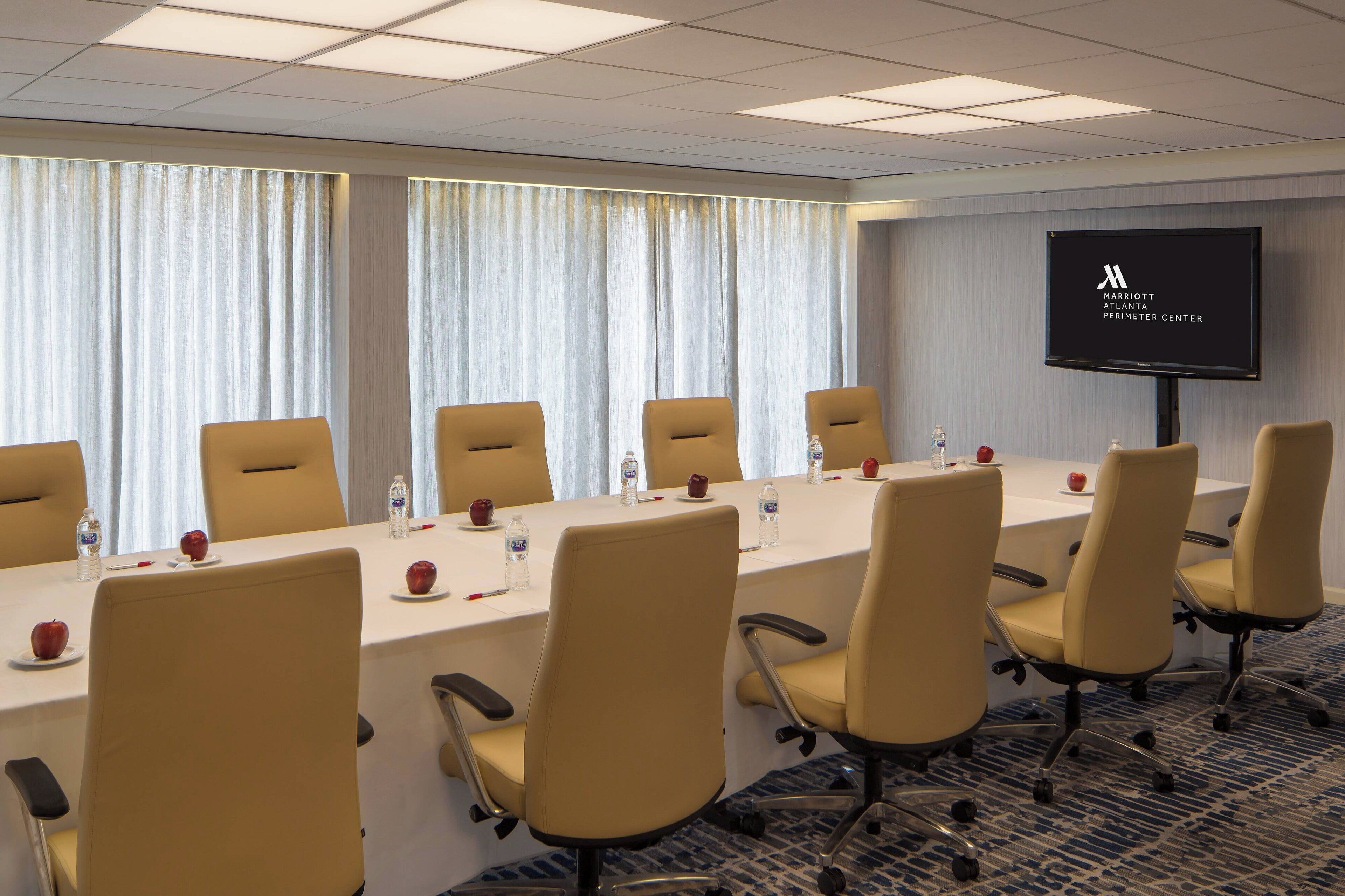 A conference room with a long table, chairs, a screen, and a water bottle on the table.