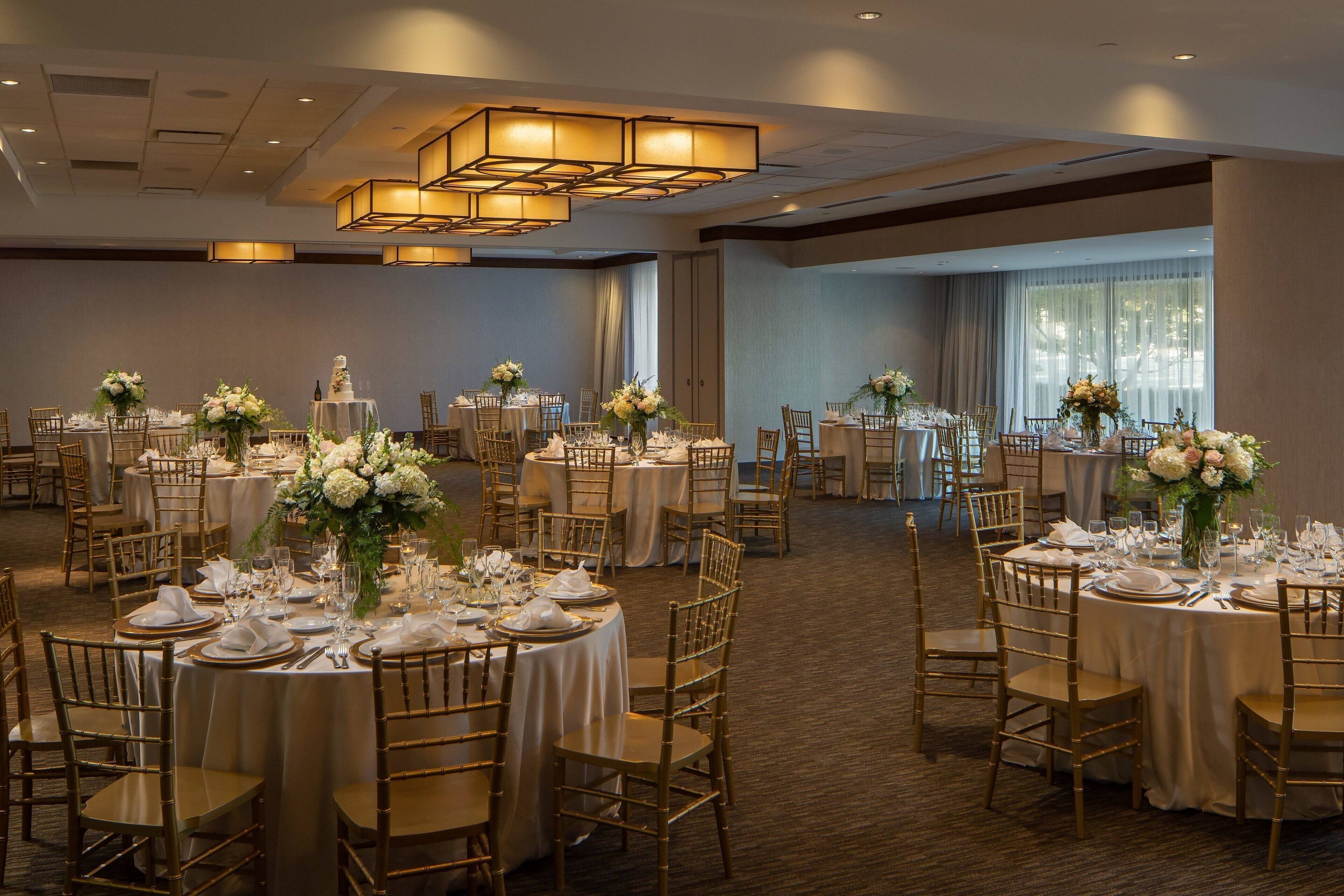 A banquet hall with round tables set for events, featuring gold chairs and white tablecloths.