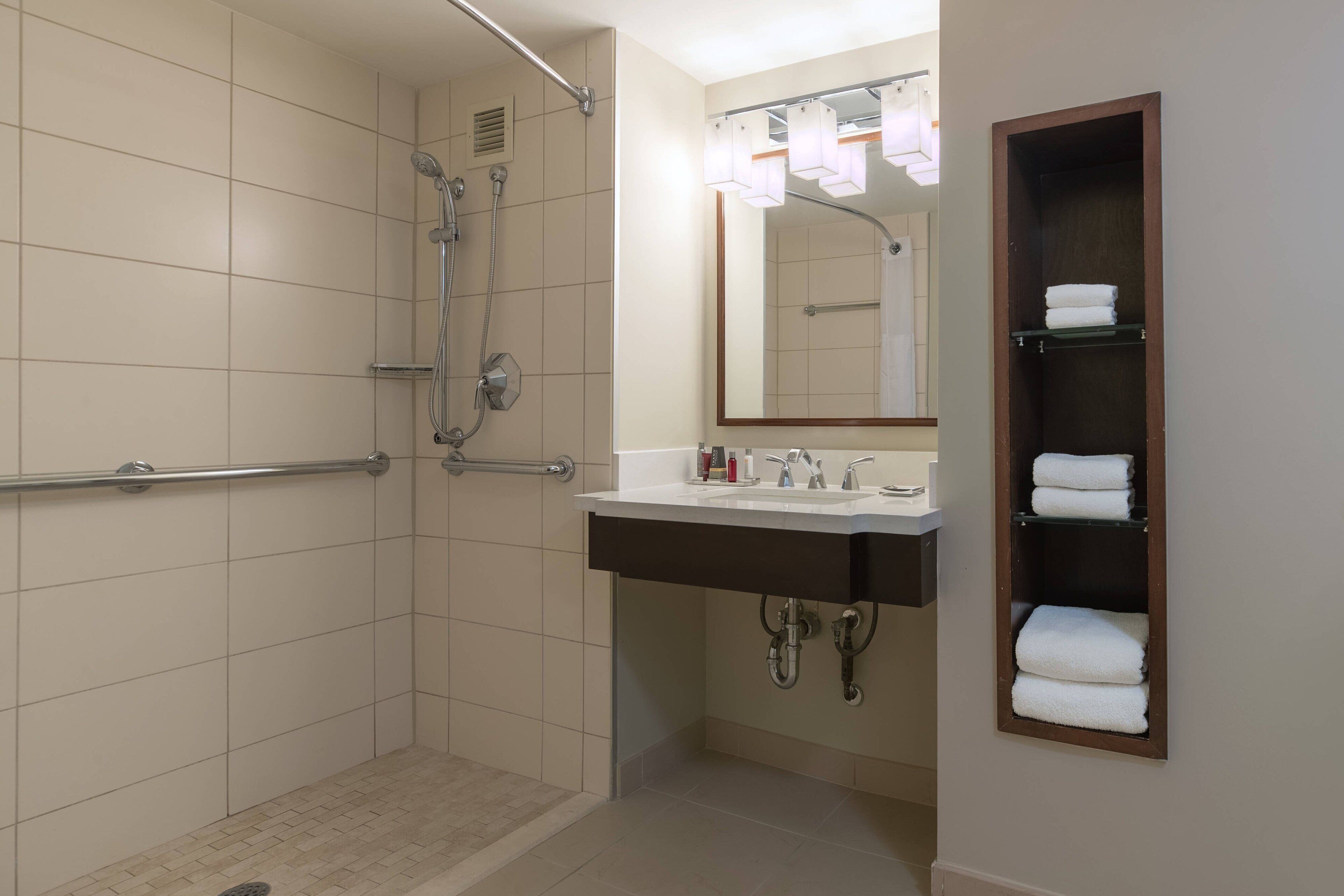 Un baño con ducha a nivel, un lavabo con espejo y un perchero para toallas.