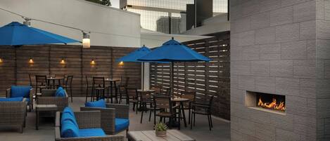 An outdoor patio with wicker furniture, blue cushions, and a built-in fire feature.