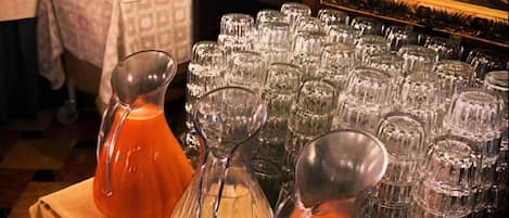 A buffet setup with multiple glassware and pitchers, a self-service beverage machine, and a mirror reflecting a person.