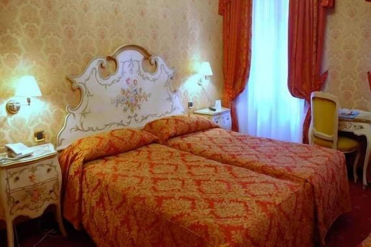 Una habitación de hotel con una cama doble, dos mesitas de noche, un escritorio con una silla y una ventana con cortinas.