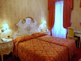 A hotel room with a double bed, two bedside tables, a desk with a chair, and a window with curtains.