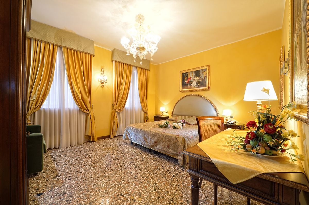 A hotel room with two beds, a chandelier, a painting on the wall, and a table with flowers.