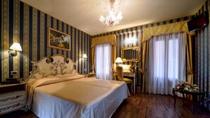 Een klassieke hotelkamer met een groot bed, een bureau, een stoel, een kaptafel met spiegel en een kroonluchter.