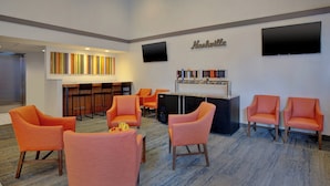Un hall d’hôtel avec des fauteuils orange, un coin bar et un téléviseur à écran plat fixé au mur.