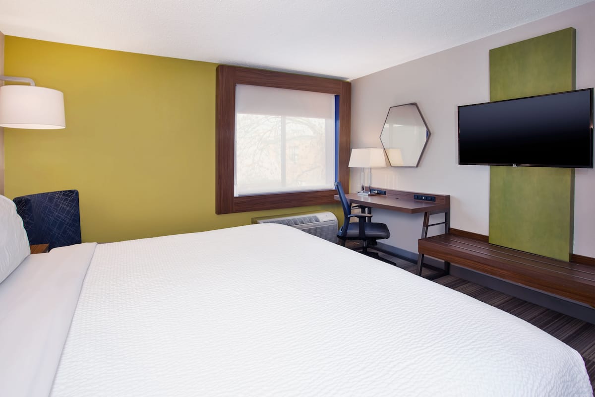 Une chambre d’hôtel avec un grand lit, un bureau avec une chaise, un téléviseur à écran plat et une fenêtre avec des stores.