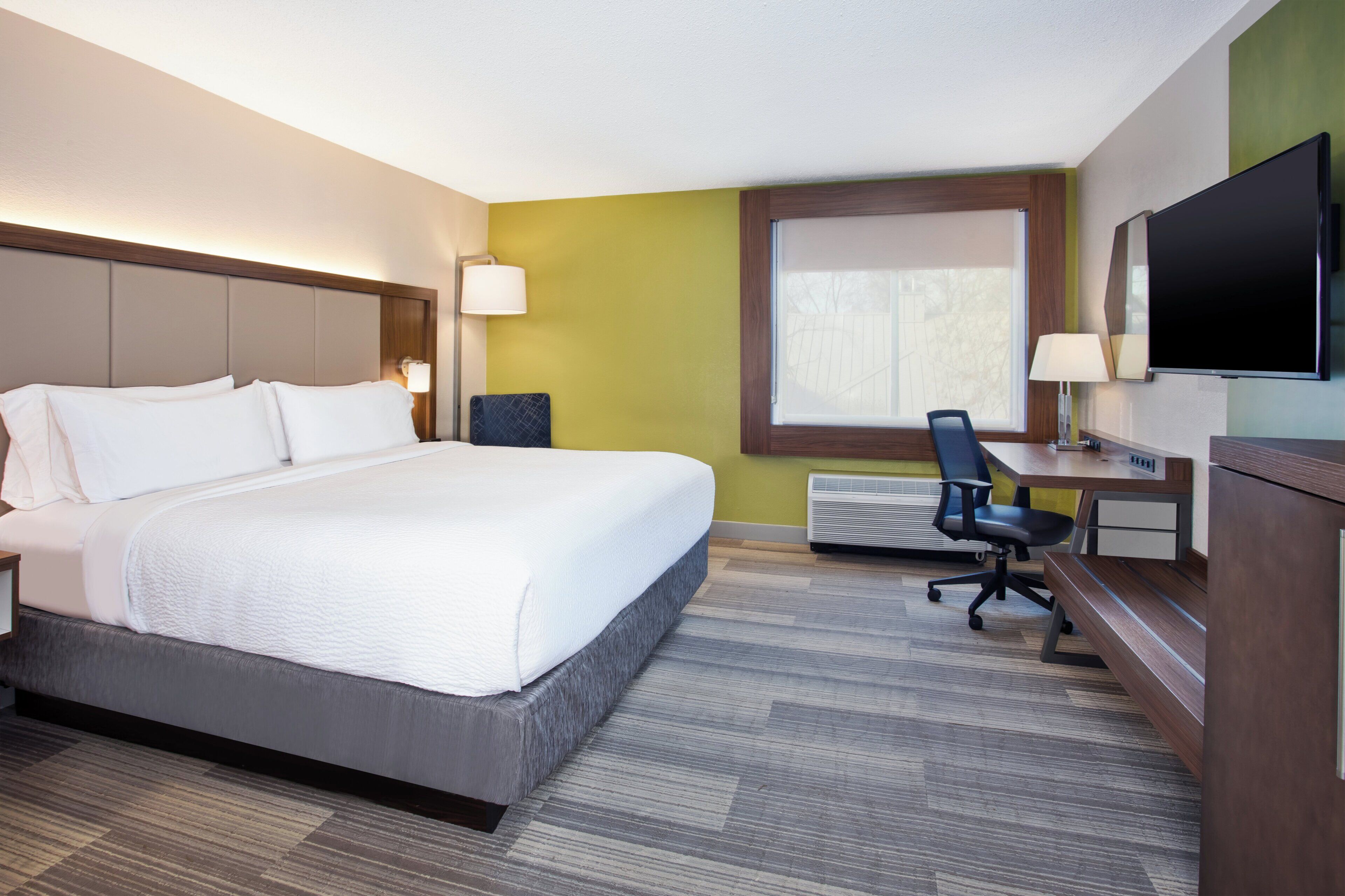 A hotel room with a large bed, a desk with a chair, a television, and a window.