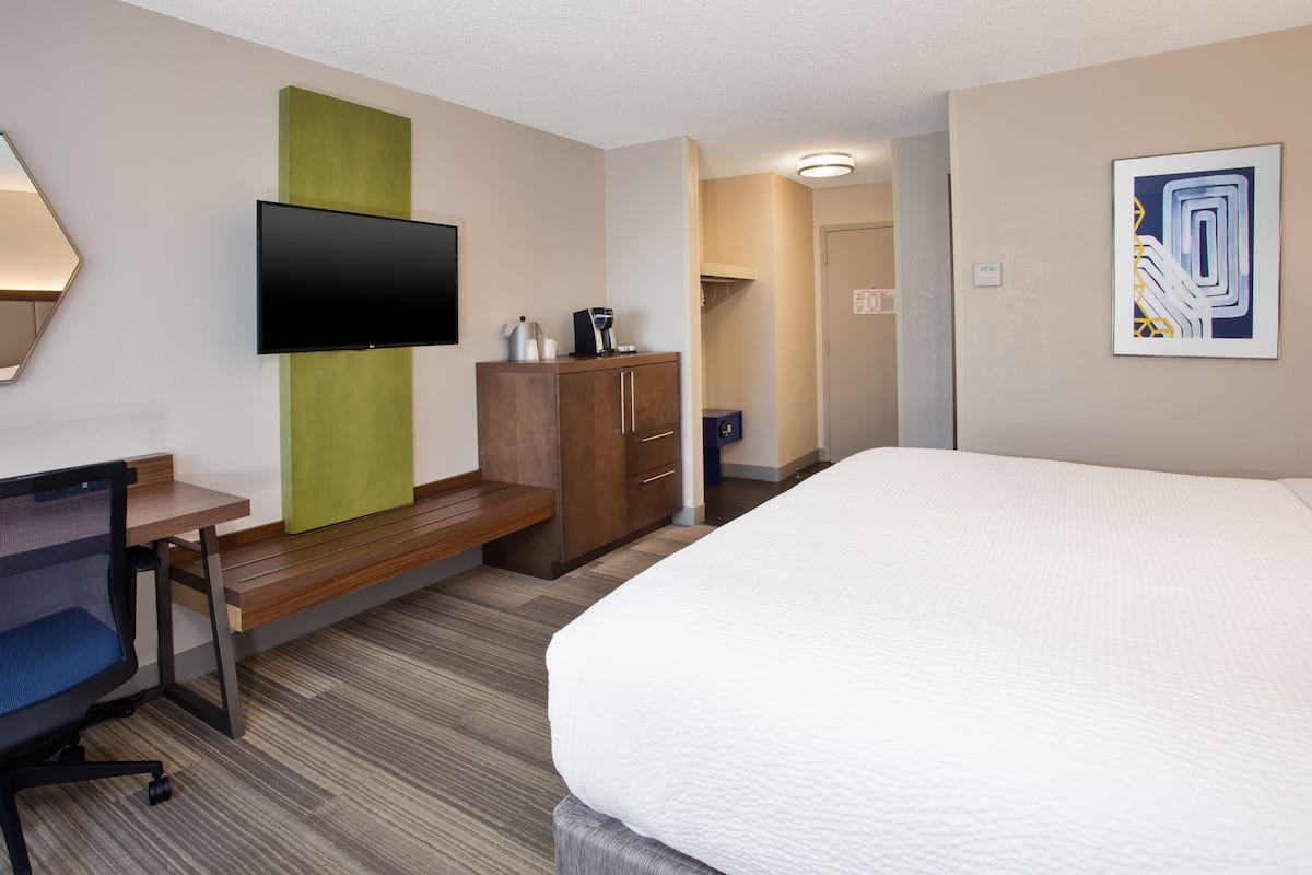 Une chambre d’hôtel comprenant un lit, un bureau avec une chaise, une télévision, une armoire et un tableau au mur.