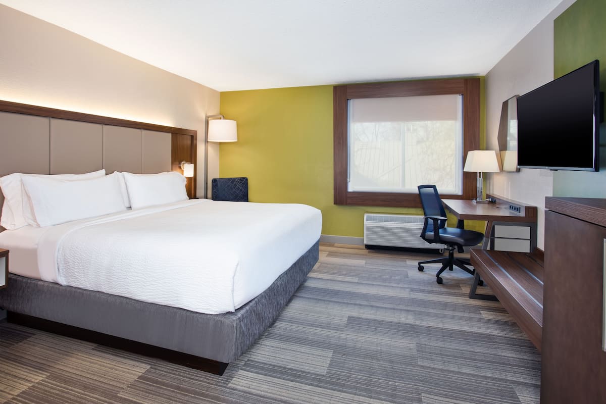 Une chambre d’hôtel avec un grand lit, un bureau avec une chaise, un téléviseur à écran plat et une fenêtre avec des stores.