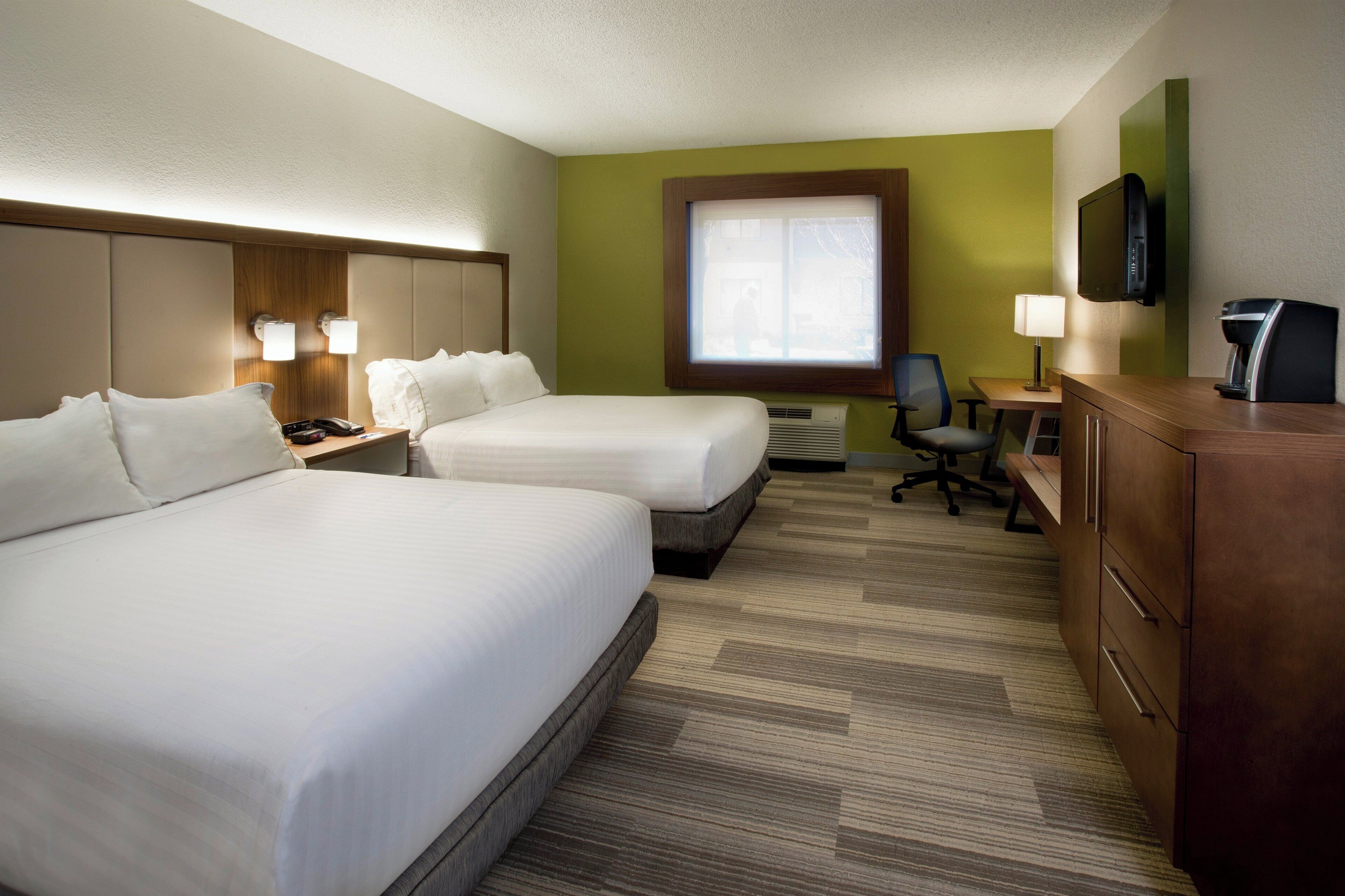 A hotel room with two beds, a desk, a chair, a TV, and a coffee maker.