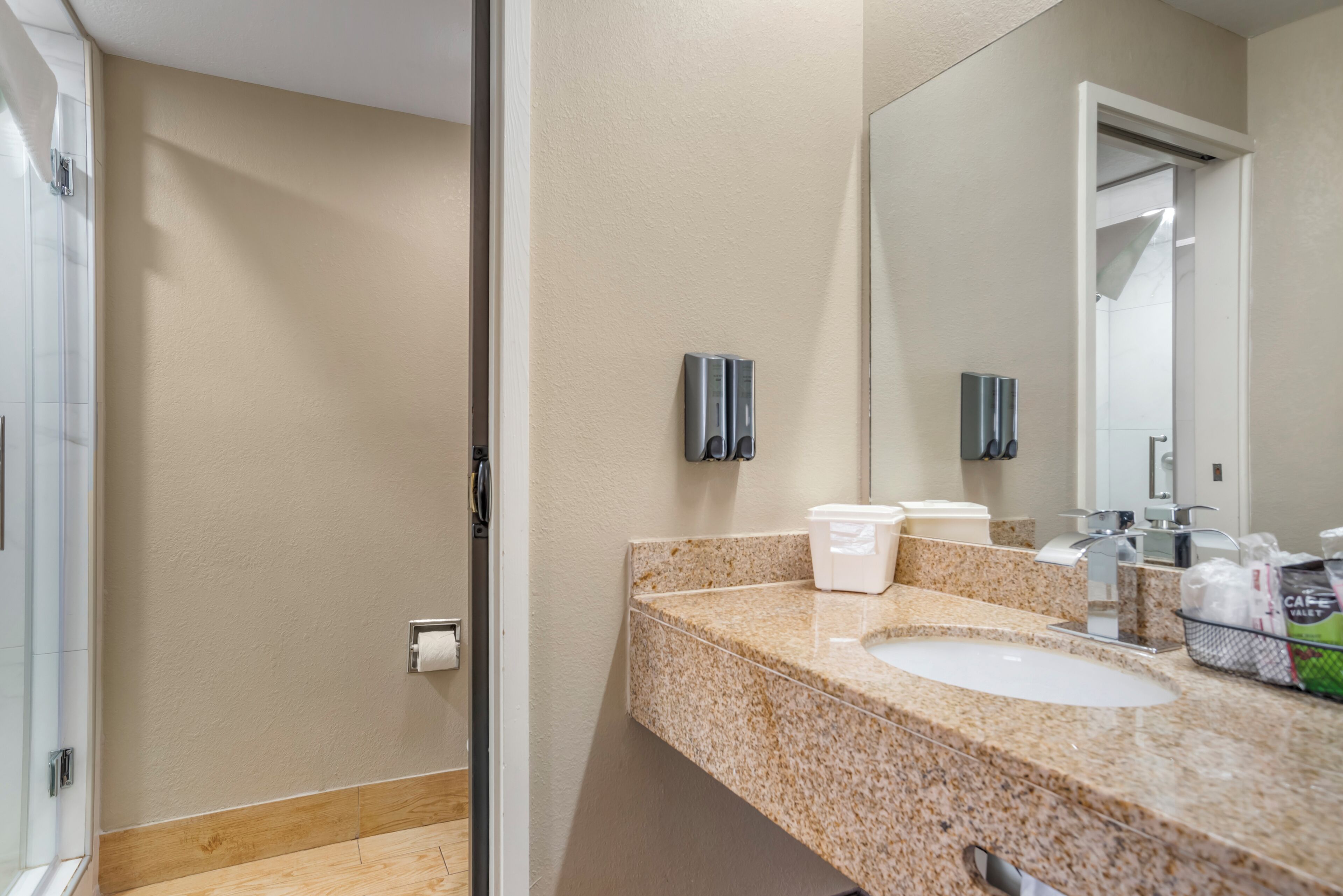 A bathroom with a granite countertop, a sink, a mirror, and a towel dispenser.