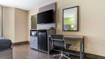 A hotel room with a bed, a desk, a chair, a television, a mini-fridge, and a mirror.