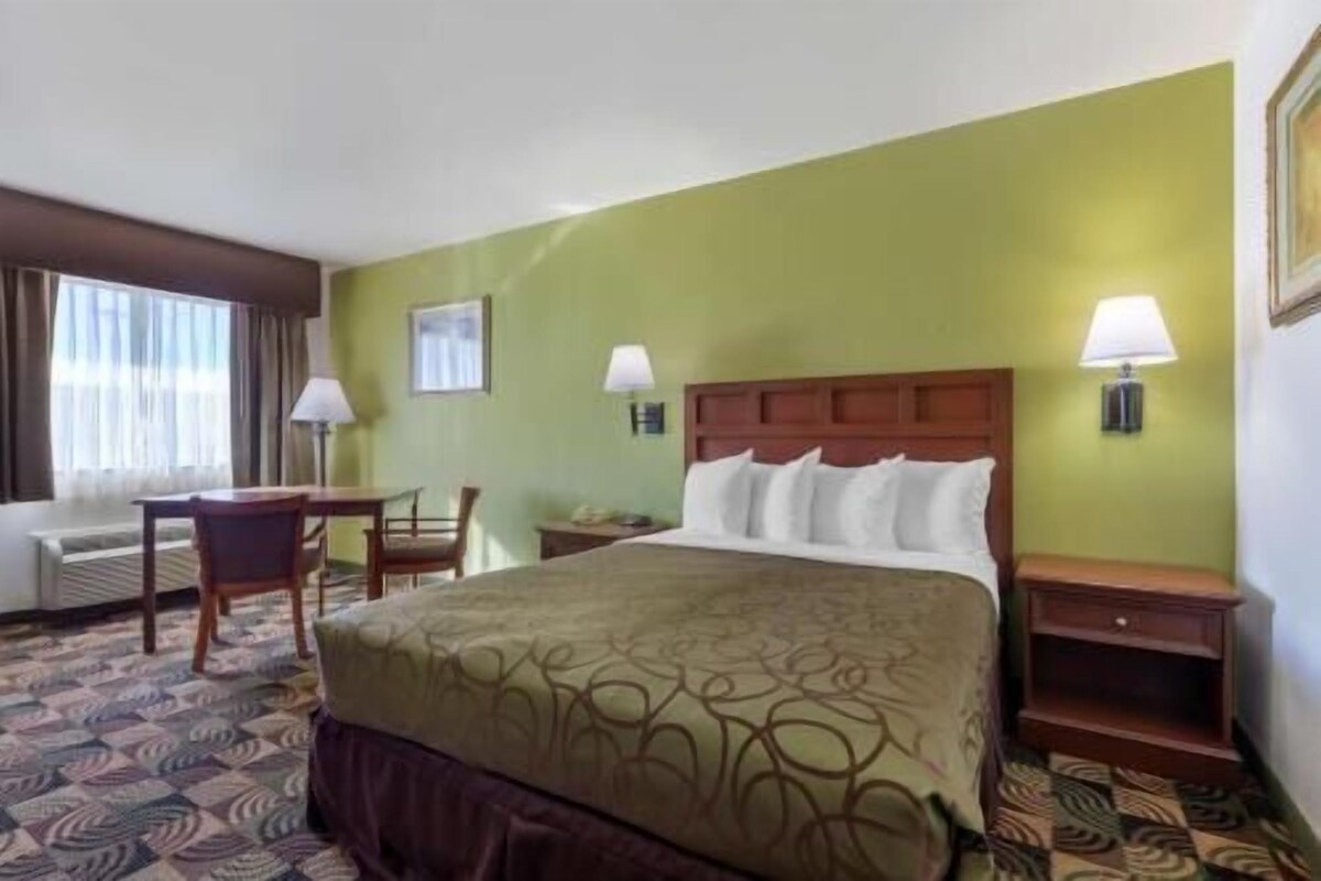 A hotel room with a bed, two bedside tables, a chair, a desk, and a window with curtains.