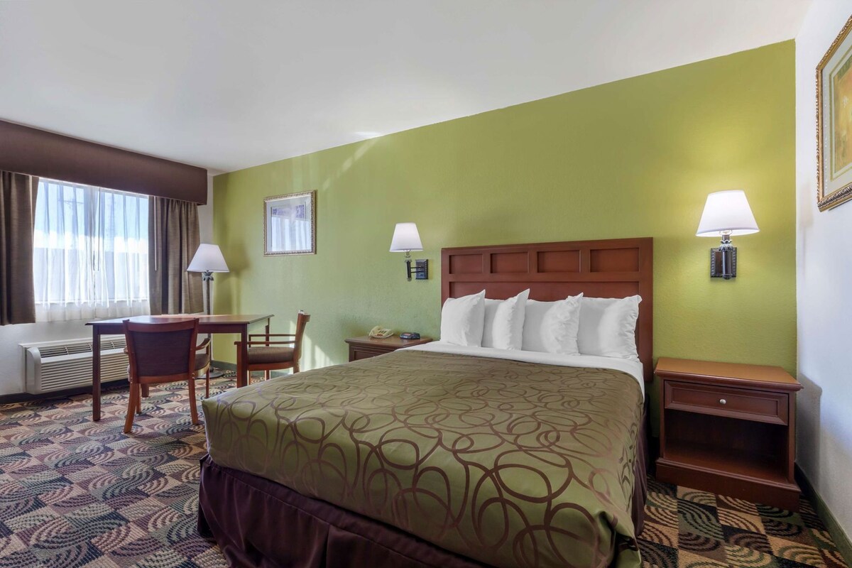 A hotel room with a large bed, a desk, a chair, a lamp, and a telephone.