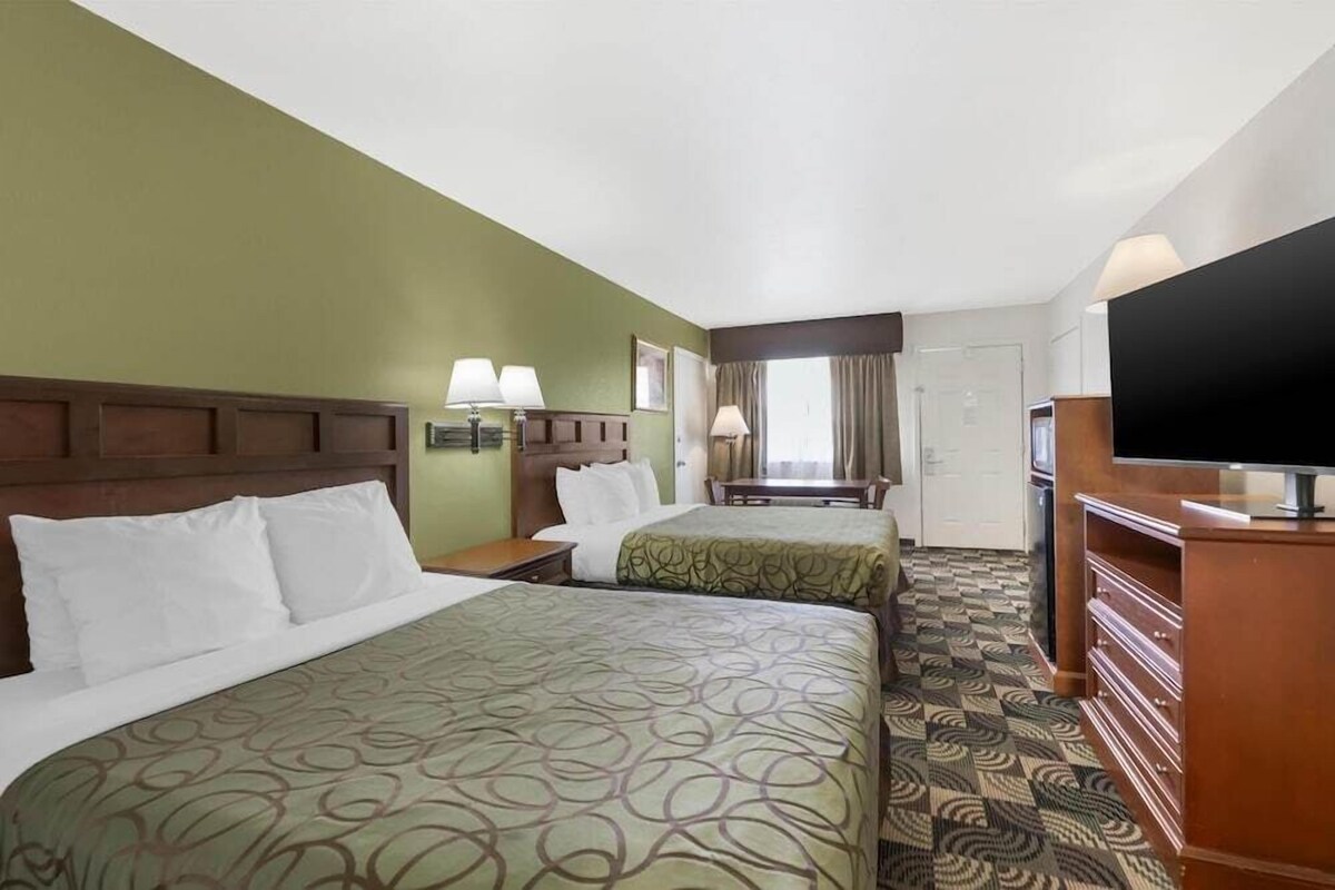 A hotel room with two beds, a television, a desk, and a window with curtains.