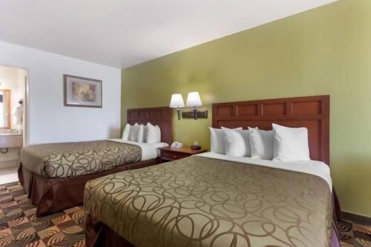 A hotel room with two beds, a nightstand, a lamp, and a framed picture on the wall.