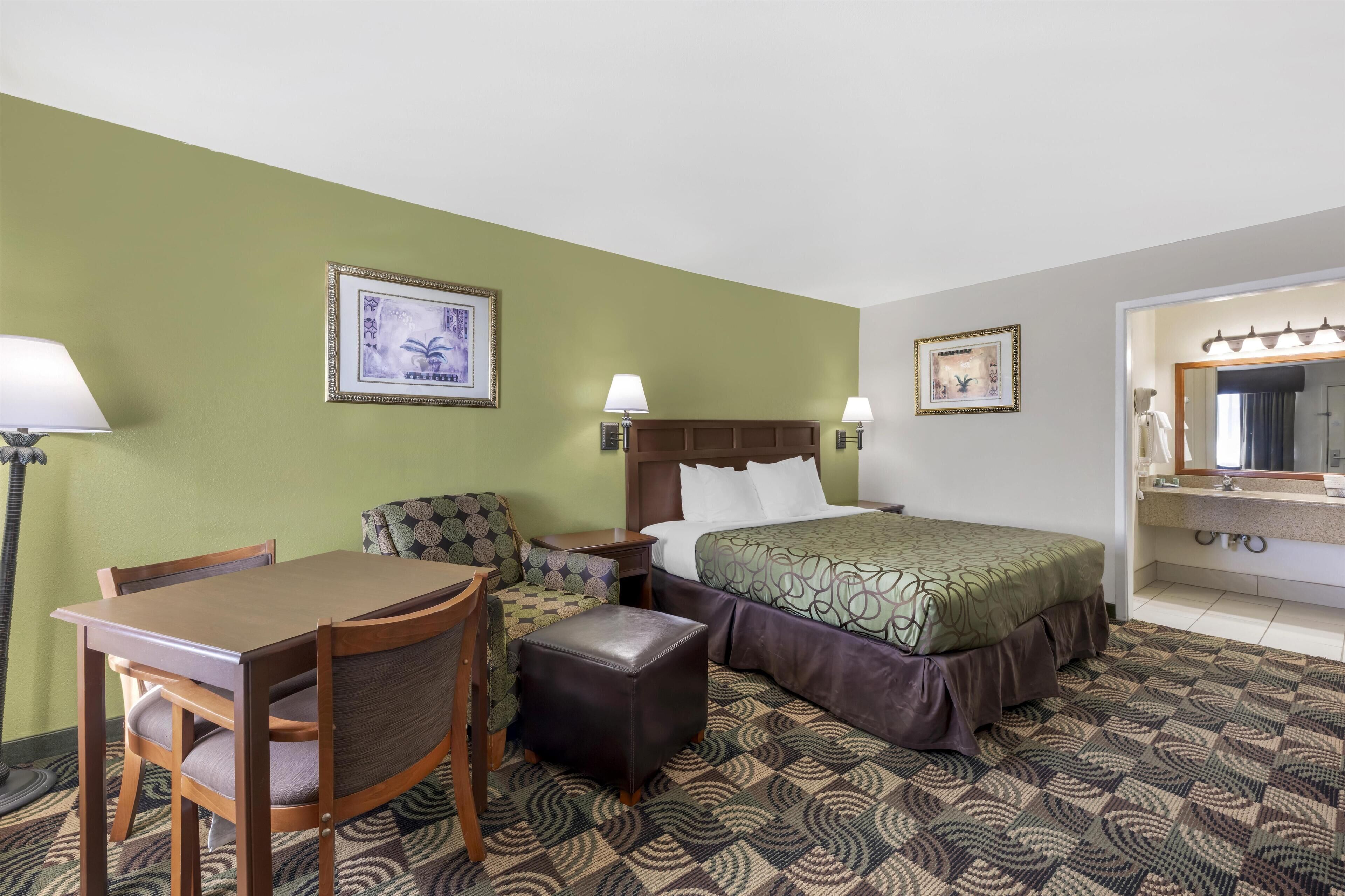Una camera d'albergo con un letto, una scrivania con sedia, un tavolino, una lampada e un tappeto decorato.