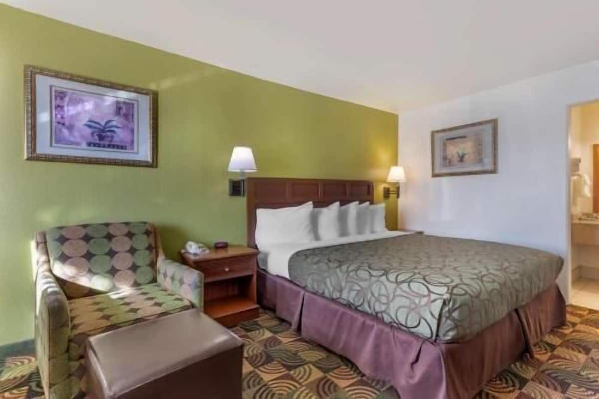 A hotel room with a bed, a chair, a nightstand, and two wall-mounted lamps.
