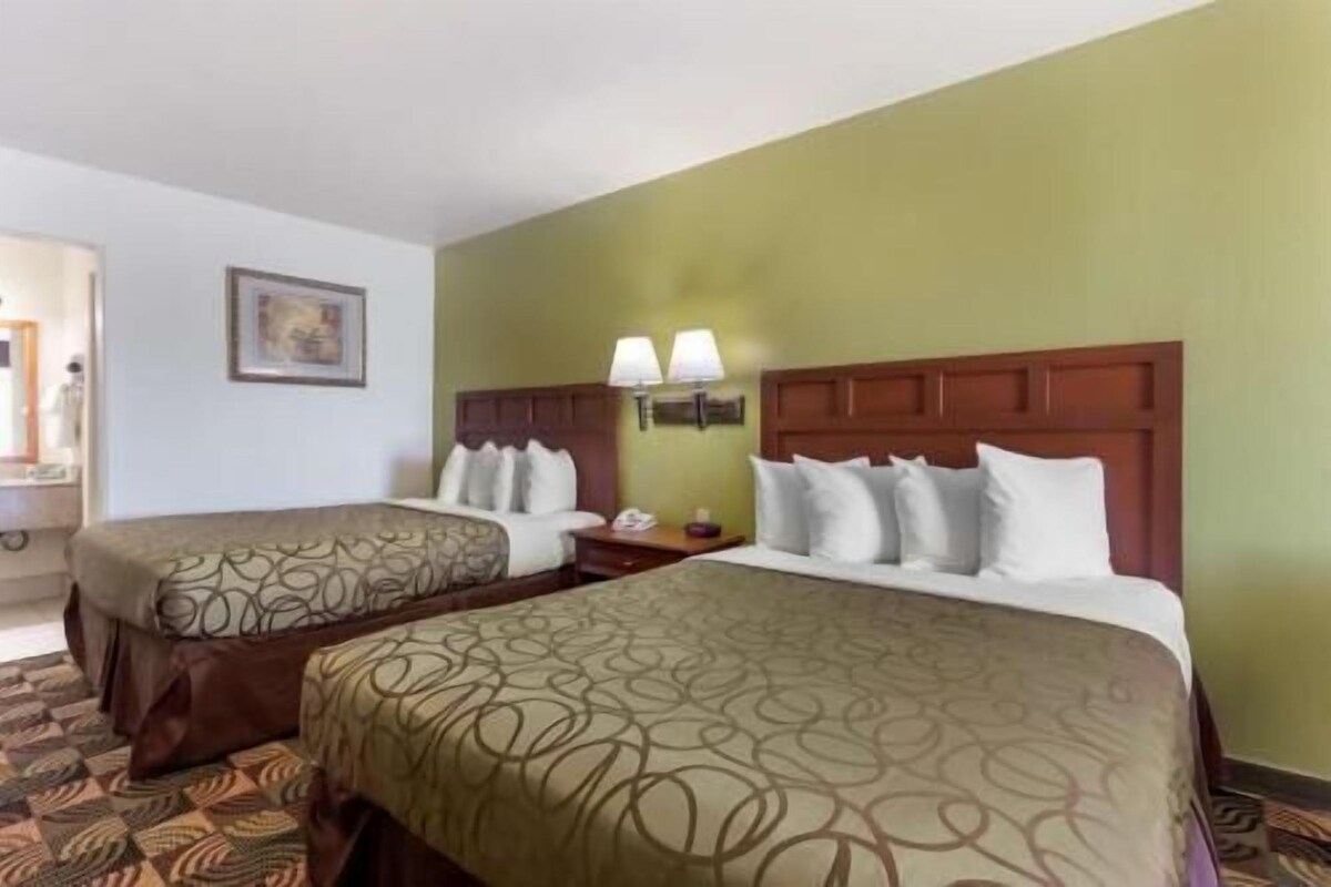 A hotel room with two beds, a nightstand, a lamp, and a framed picture on the wall.