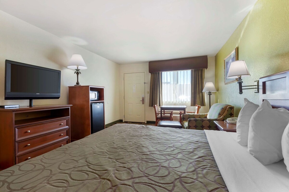 A hotel room with a bed, a television, a desk, a chair, and a window with curtains.