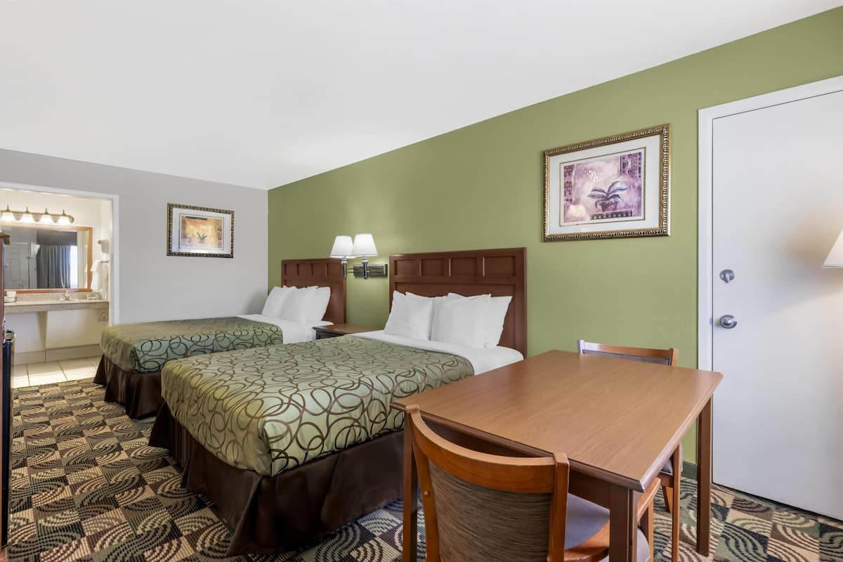 A hotel room with two beds, a wooden table, and a mirror.