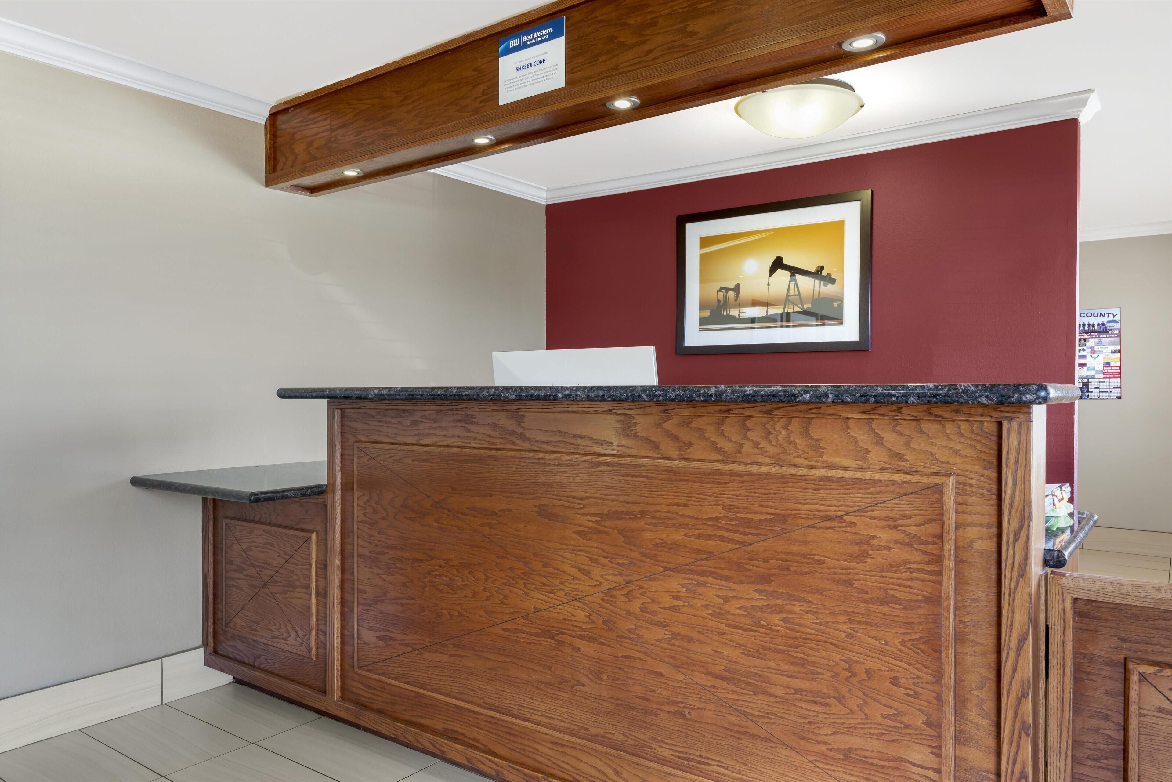 A reception desk with a wooden finish, a framed picture on the wall, and a sign above it.