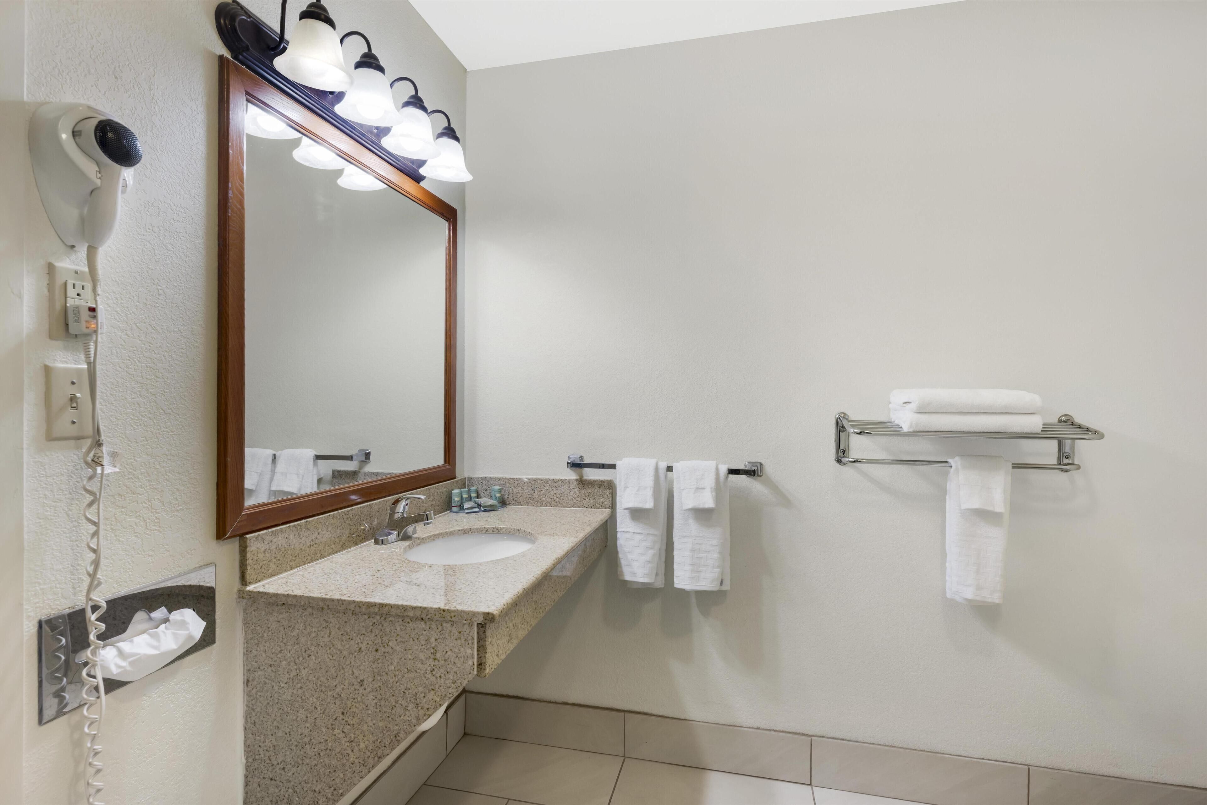 Un baño con lavamanos, espejo, secador de pelo y toallero.
