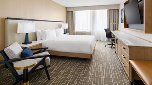 A hotel room with a large bed, a desk, a chair, a TV, and a window with curtains.