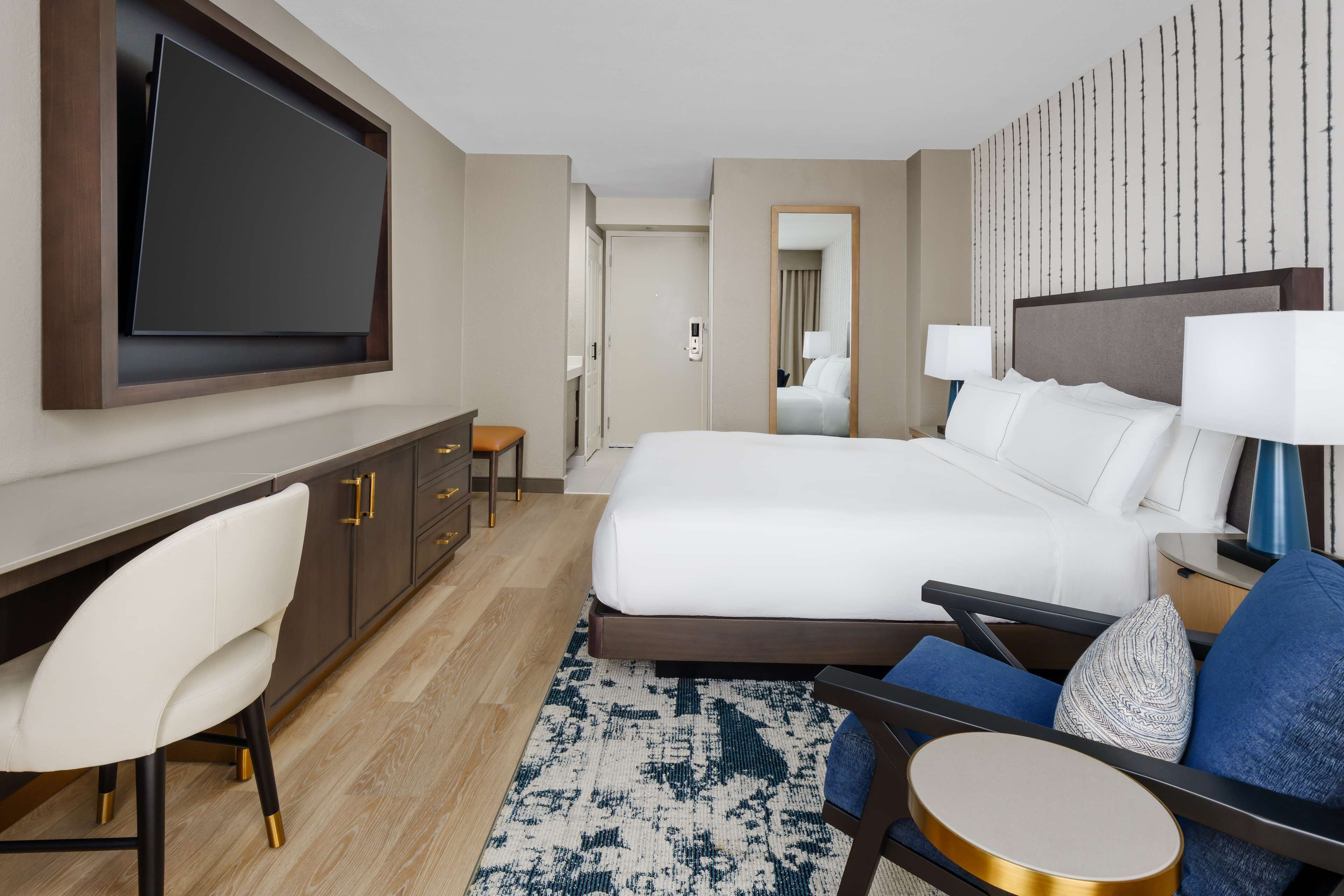 Une chambre d’hôtel avec un grand lit, un bureau avec une chaise, un téléviseur fixé au mur et une table de chevet avec des lampes.
