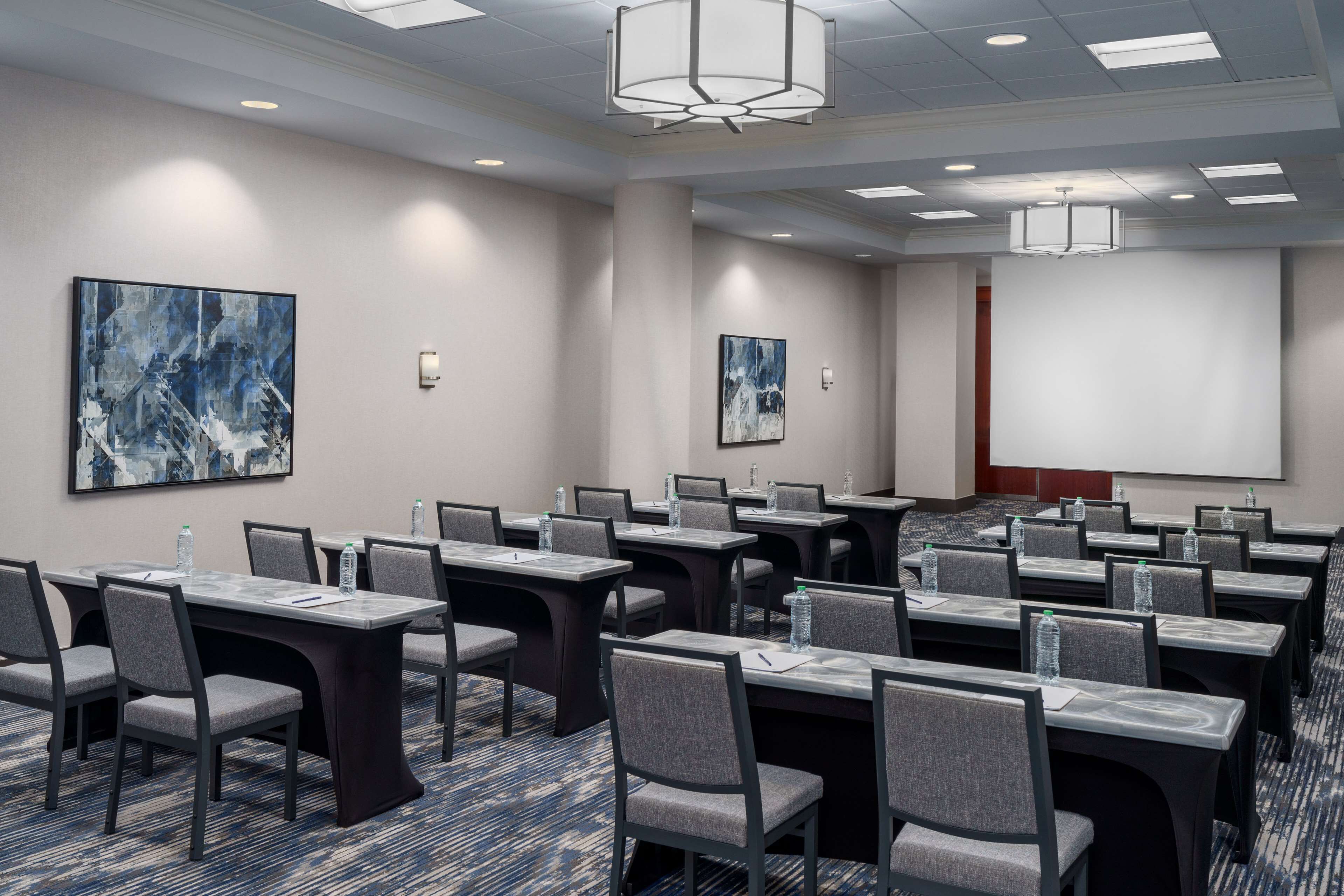 A conference room with multiple tables and chairs, equipped with water bottles and presentation screens.