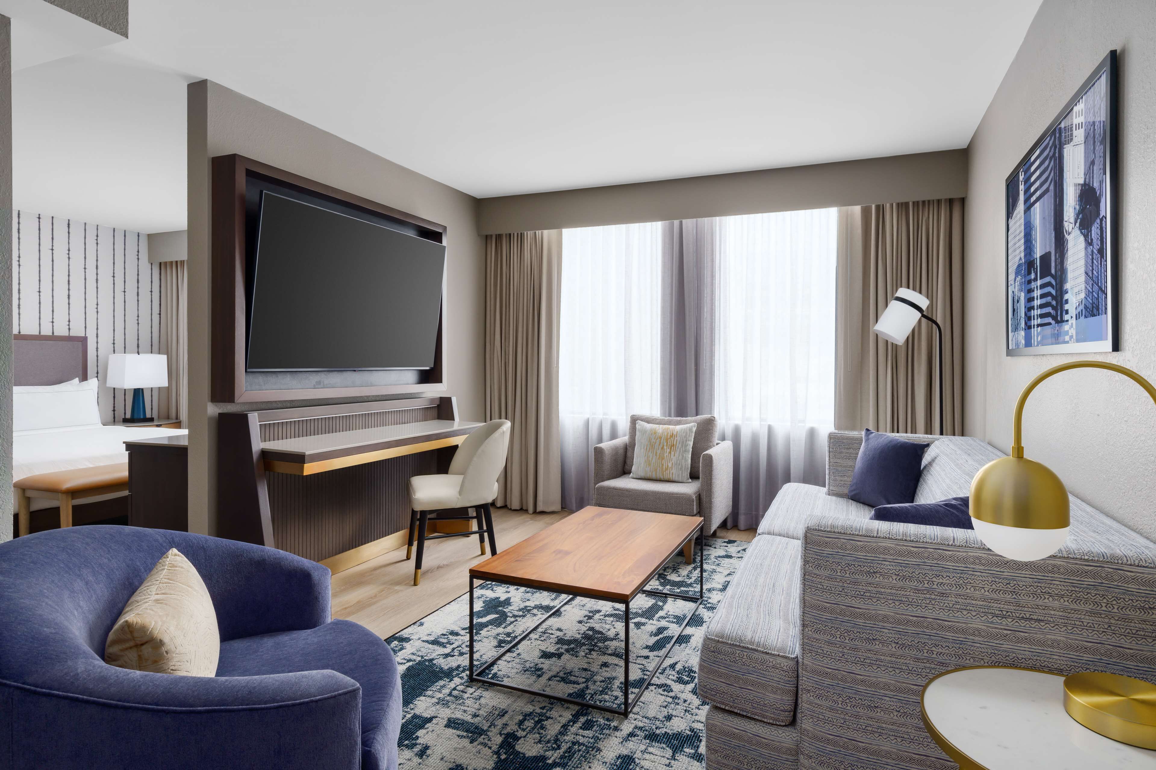 A modern hotel room with a flat-screen TV, a desk, a sofa, and a coffee table.