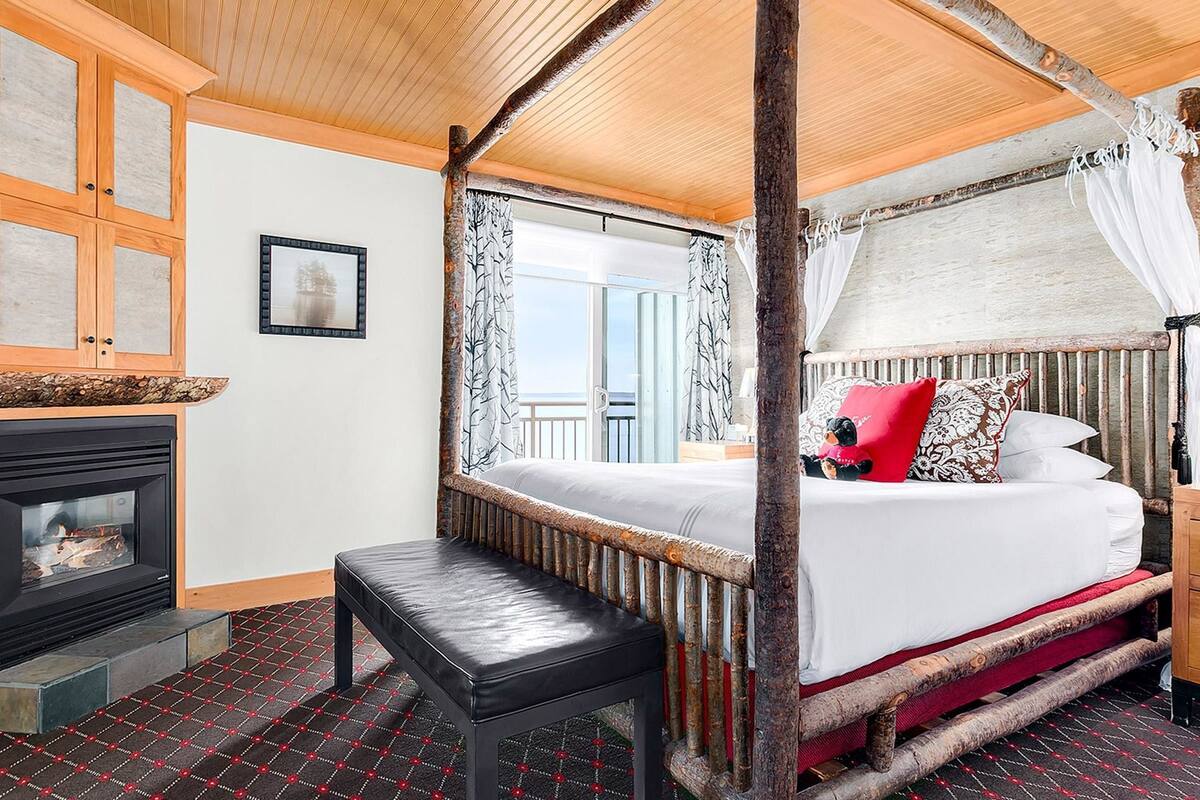 A four-poster canopy bed with a bench, a fireplace, and a view of the sea.