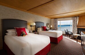 A hotel room with two beds, a desk, a chair, and a view of the sea.
