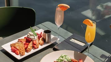 A table with a plate of food and two drinks, a glass of orange juice, and a glass of champagne, with a view of the water in the background.